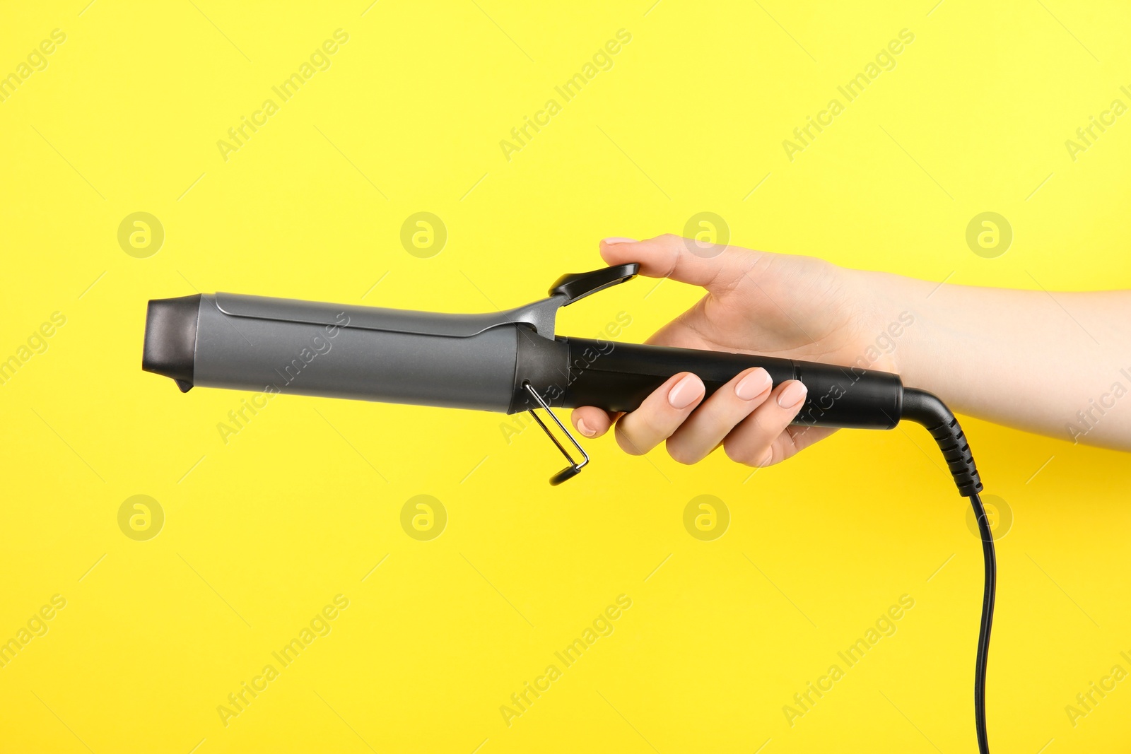 Photo of Hair styling appliance. Woman holding curling iron on yellow background, closeup