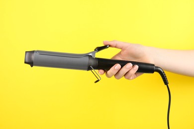 Hair styling appliance. Woman holding curling iron on yellow background, closeup