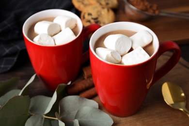 Composition of tasty cocoa with marshmallows in cups on wooden table