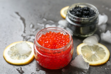 Glass jars with black and red caviar on grey background