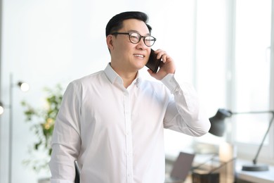 Photo of Portrait of smiling businessman talking by smartphone in office