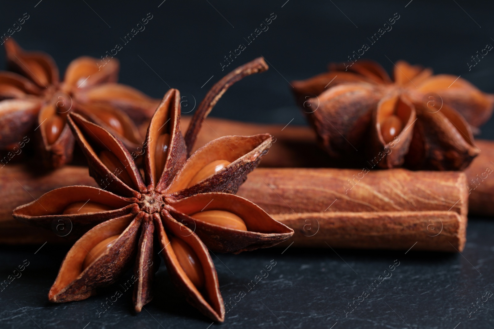 Photo of Aromatic anise stars and cinnamon sticks on black table, closeup