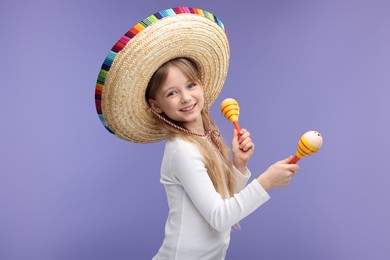 Photo of Cute girl in Mexican sombrero hat dancing with maracas on purple background