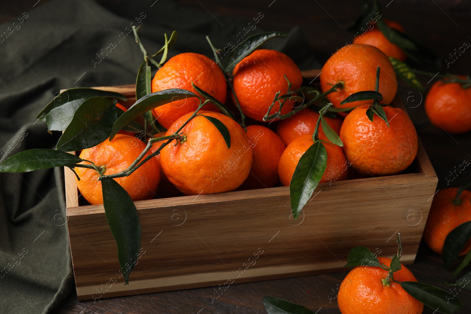 Photo of Fresh ripe tangerines with green leaves in crate on wooden table