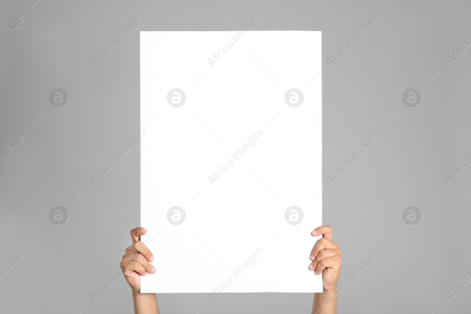 Photo of Man holding white blank poster on grey background, closeup. Mockup for design