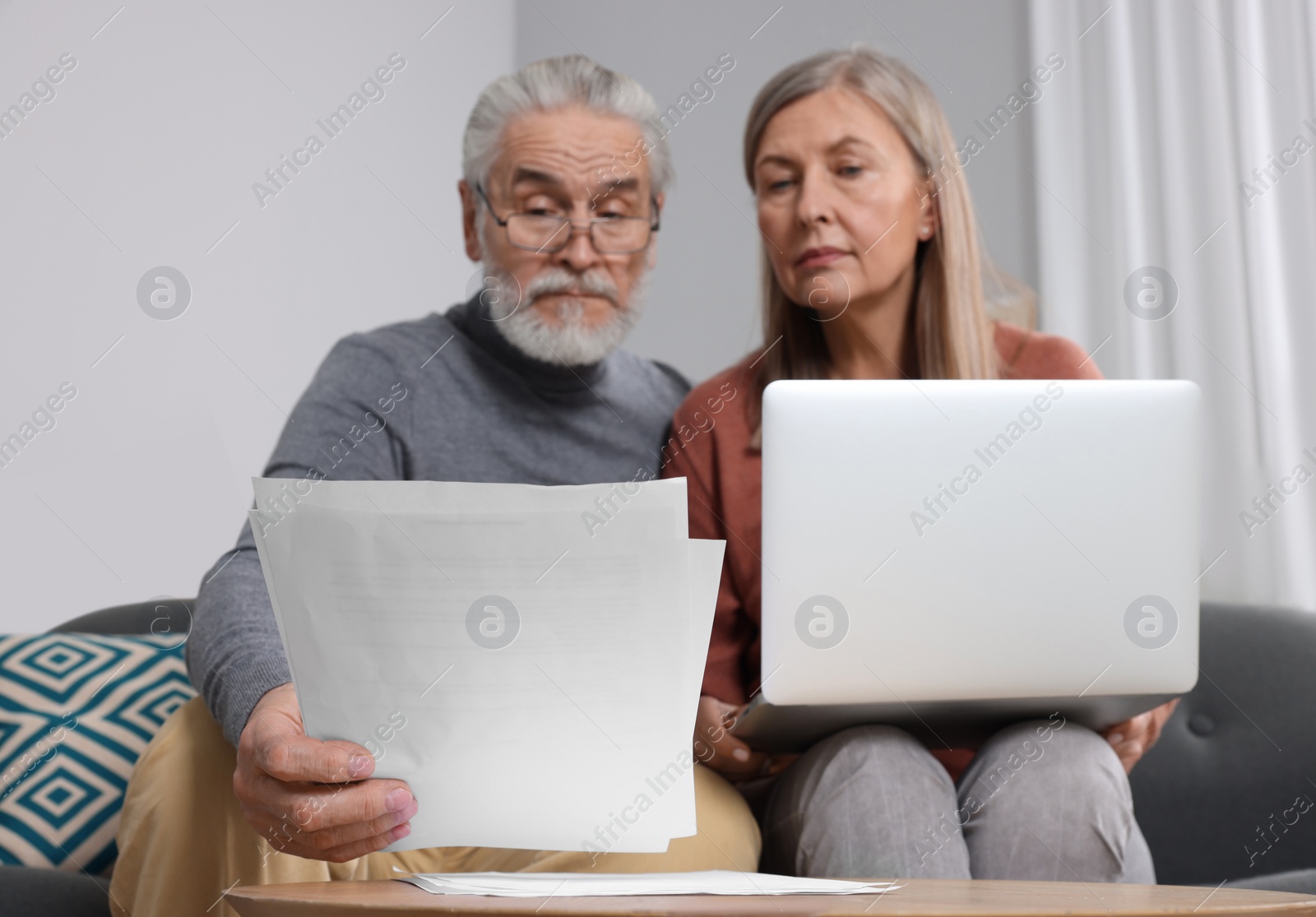 Photo of Elderly couple with papers and laptop discussing pension plan in room