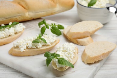 Photo of Bread with cottage cheese and basil on white wooden table, closeup