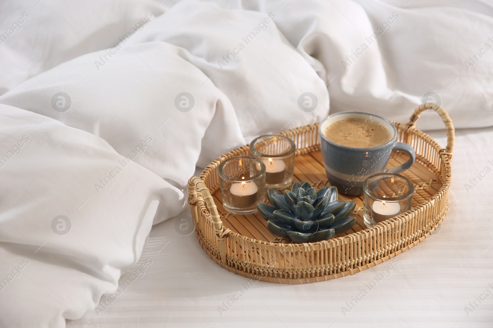 Photo of Wicker tray with cup of coffee and candles near soft blanket on bed
