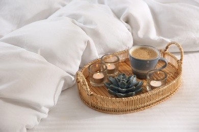 Wicker tray with cup of coffee and candles near soft blanket on bed