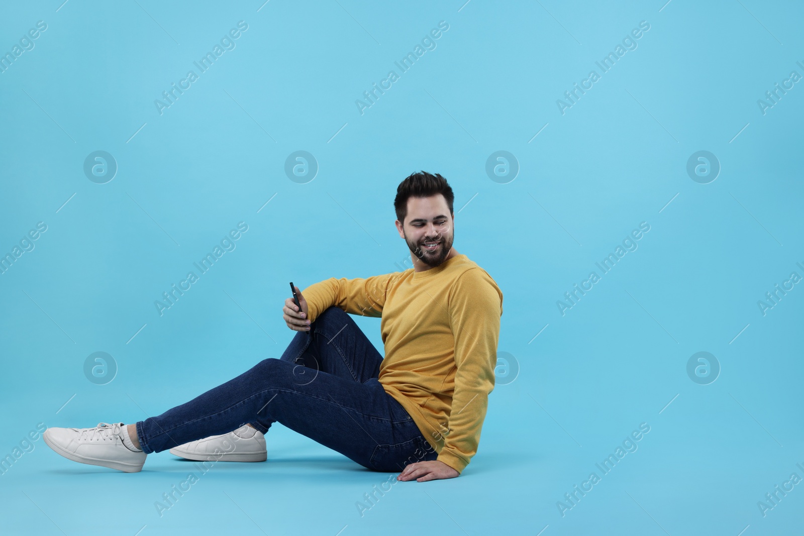 Photo of Handsome young man using smartphone on light blue background, space for text