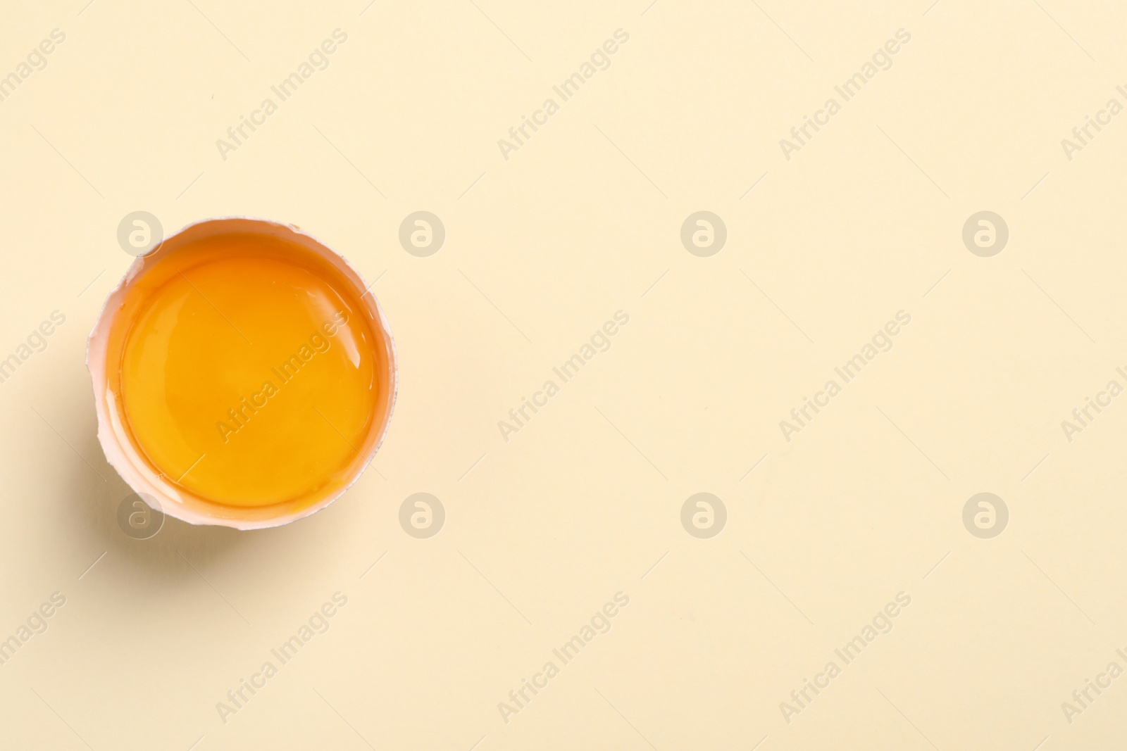 Photo of Cracked eggshell with raw yolk on beige background, top view. Space for text