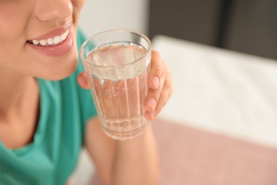 Photo of Young woman drinking pure water from glass indoors, closeup. Space for text