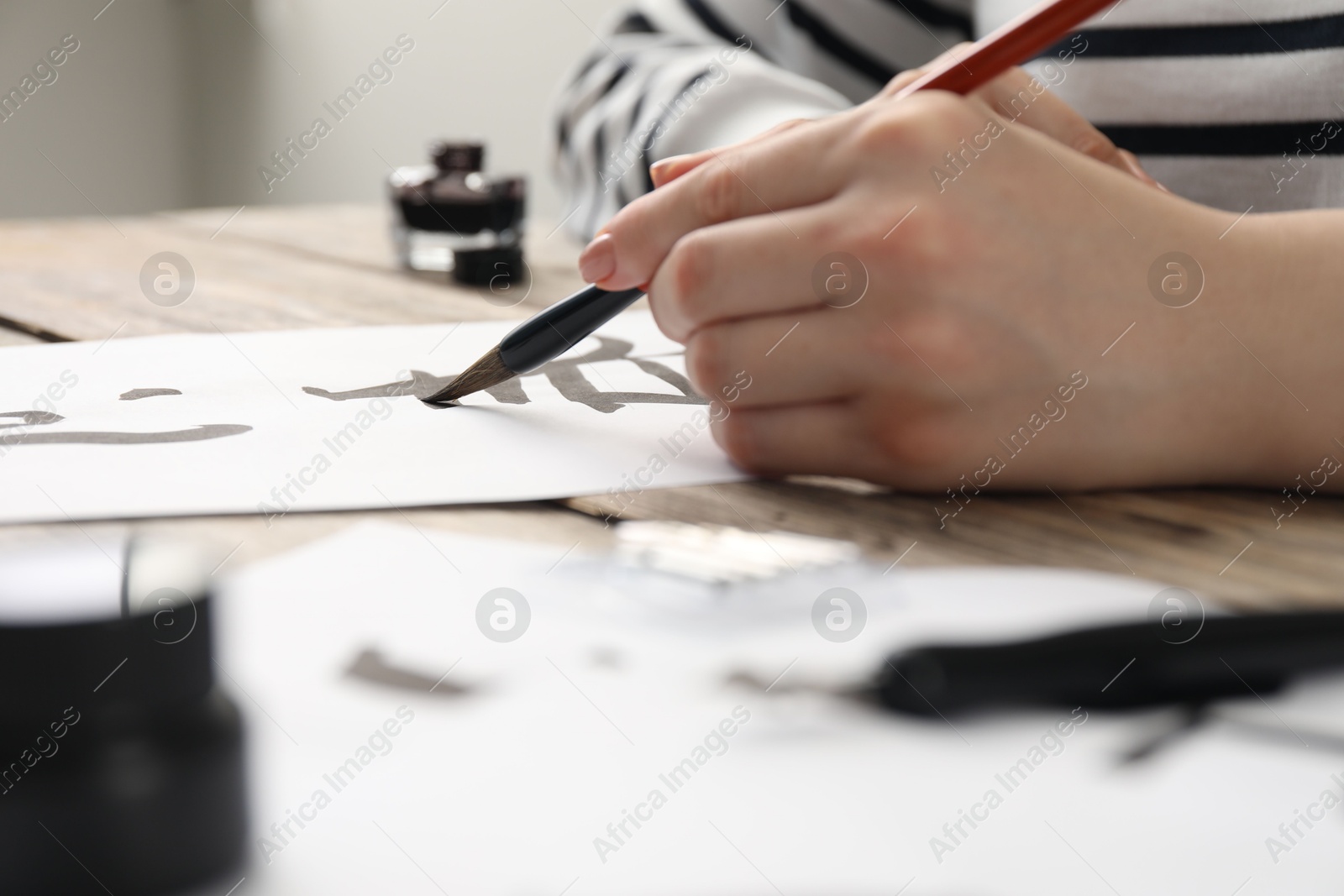 Photo of Calligraphy. Woman with brush writing hieroglyphs on paper at table, closeup