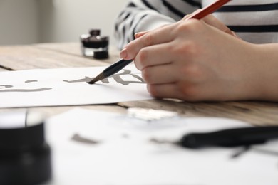 Photo of Calligraphy. Woman with brush writing hieroglyphs on paper at table, closeup