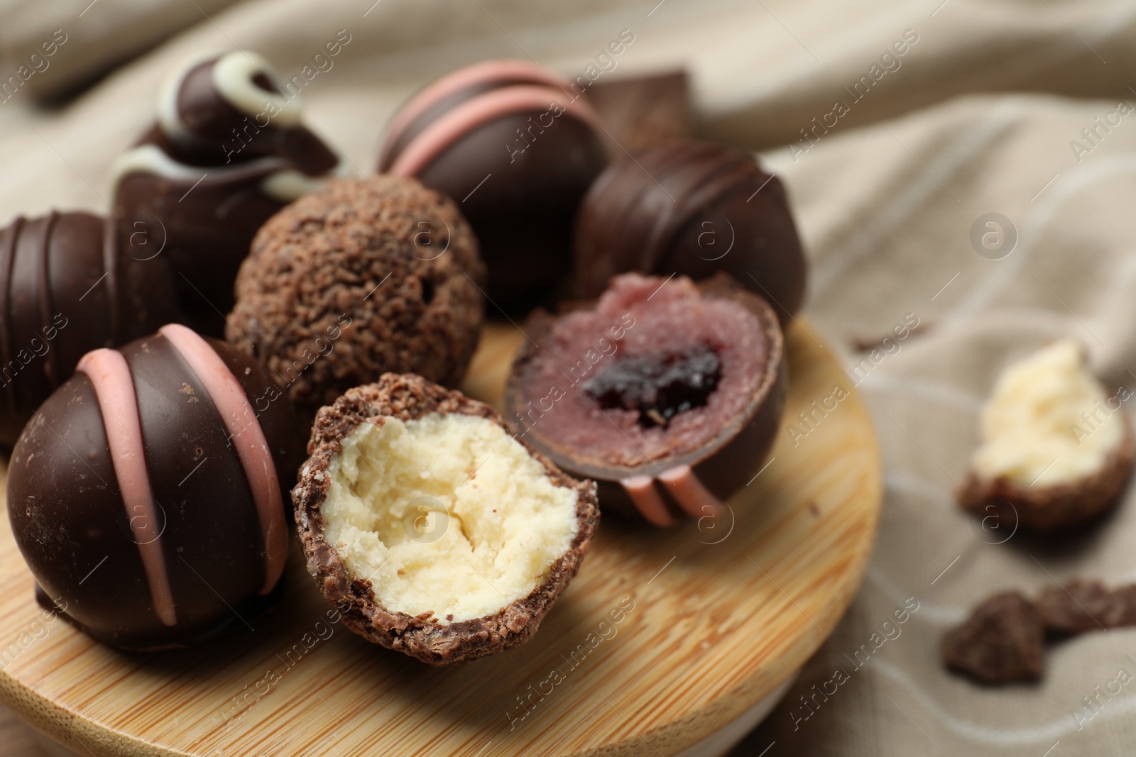 Photo of Many different delicious chocolate truffles on wooden plate, closeup