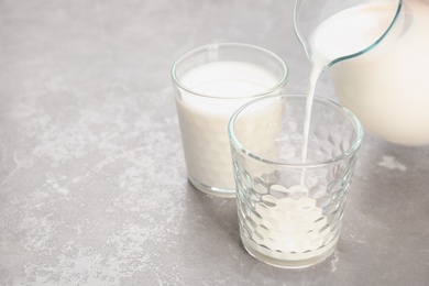 Photo of Pouring of milk from jug into glass on table. Fresh dairy product