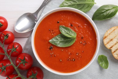 Flat lay composition with delicious tomato cream soup in bowl on white wooden table