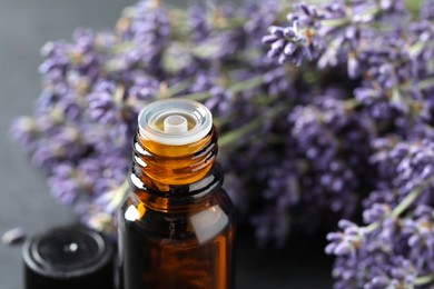 Bottle with essential oil near lavender on table, closeup