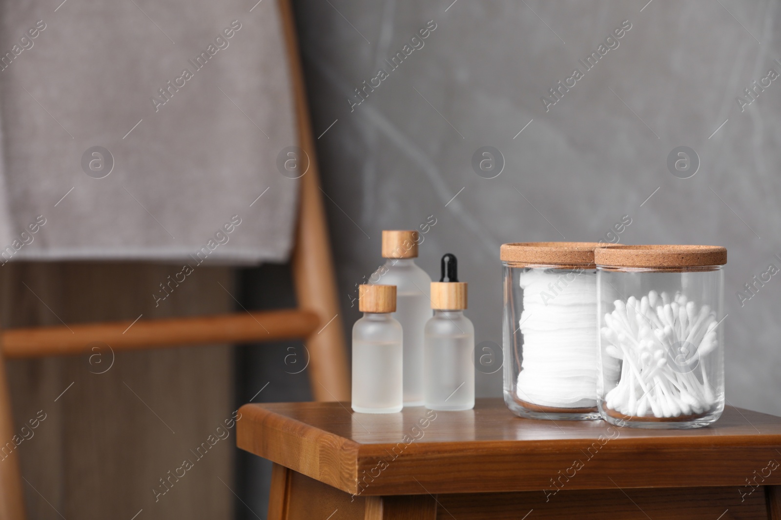 Photo of Cotton pads and swabs near cosmetic products on wooden stool in room. Space for text