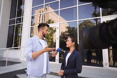 Photo of Professional journalist taking interview in front of video camera outdoors