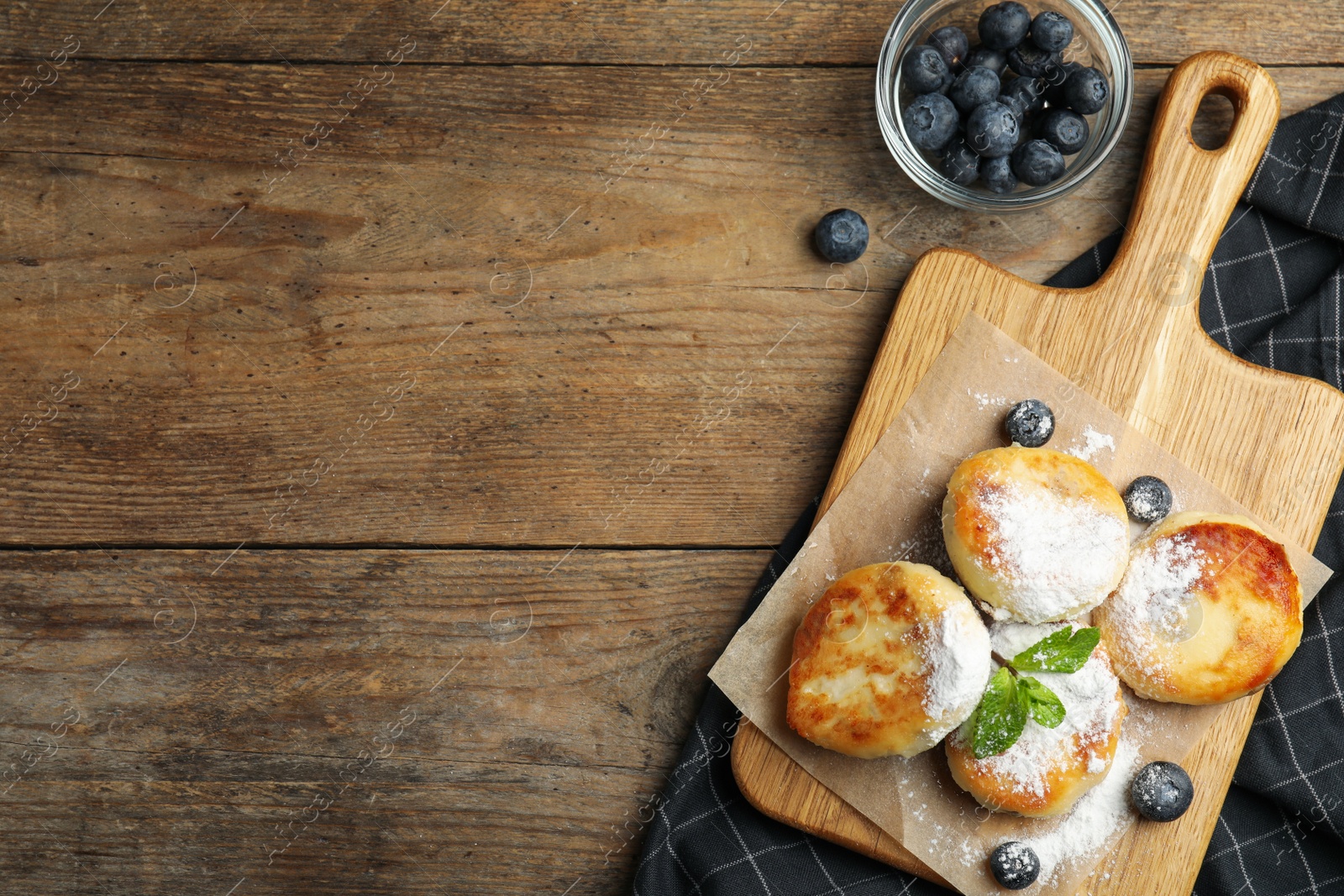 Photo of Delicious cottage cheese pancakes with blueberries and sugar powder on wooden table, flat lay. Space for text