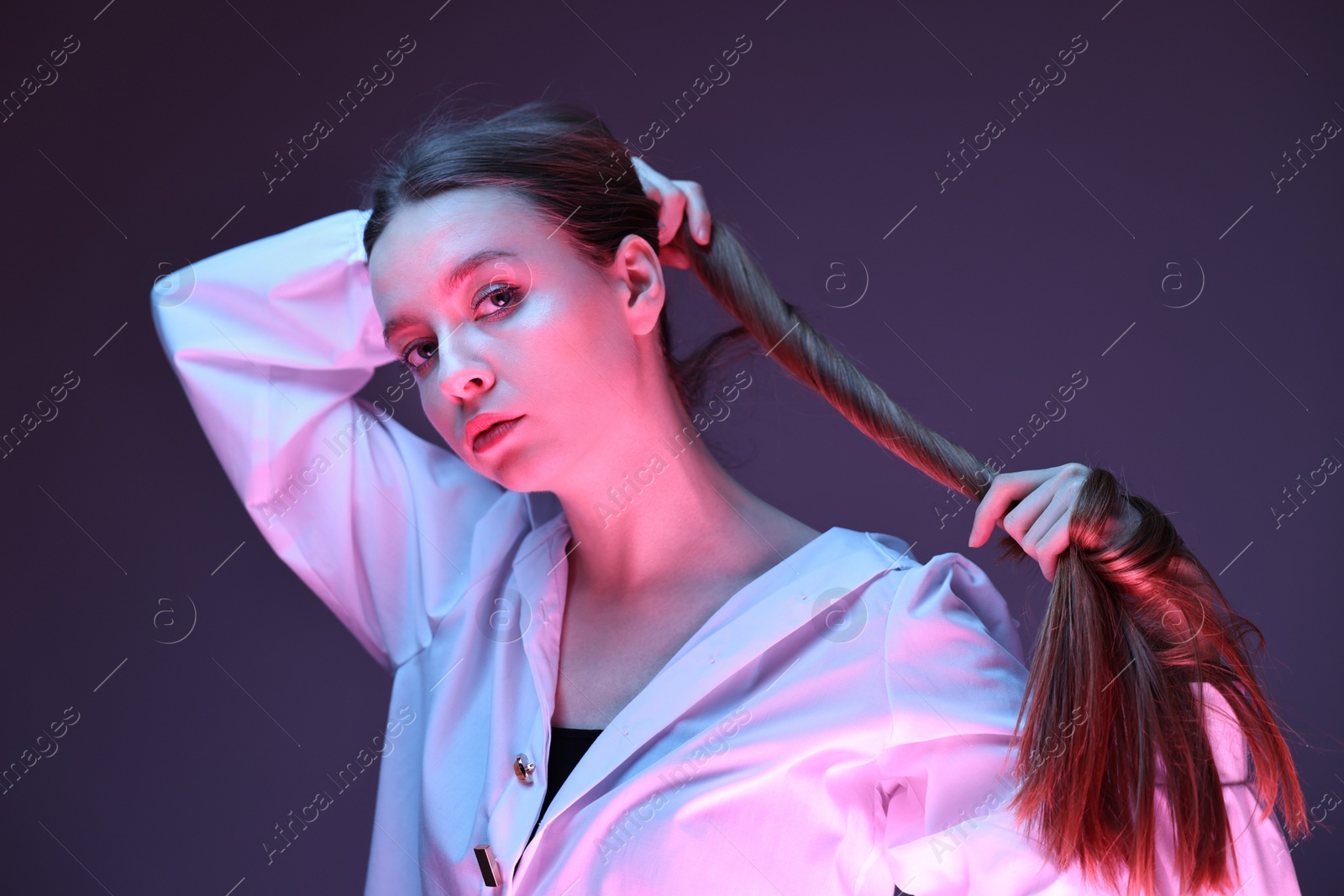 Photo of Fashionable portrait of beautiful young woman on purple background in neon lights