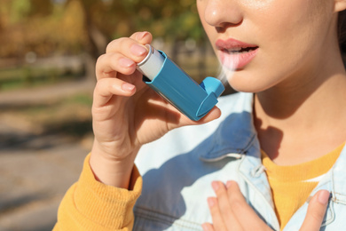 Image of Woman using asthma inhaler outdoors, closeup. Health care