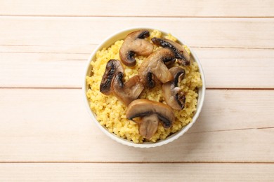 Photo of Tasty millet porridge and mushrooms in bowl on light wooden table, top view