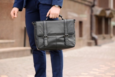 Businessman with black briefcase in hand outdoors. Space for text