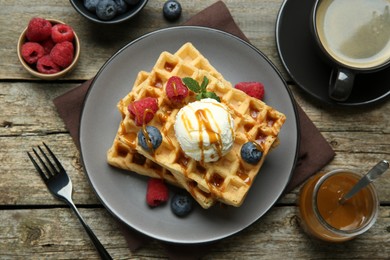 Photo of Delicious Belgian waffles with ice cream, berries and caramel sauce served on wooden table, flat lay