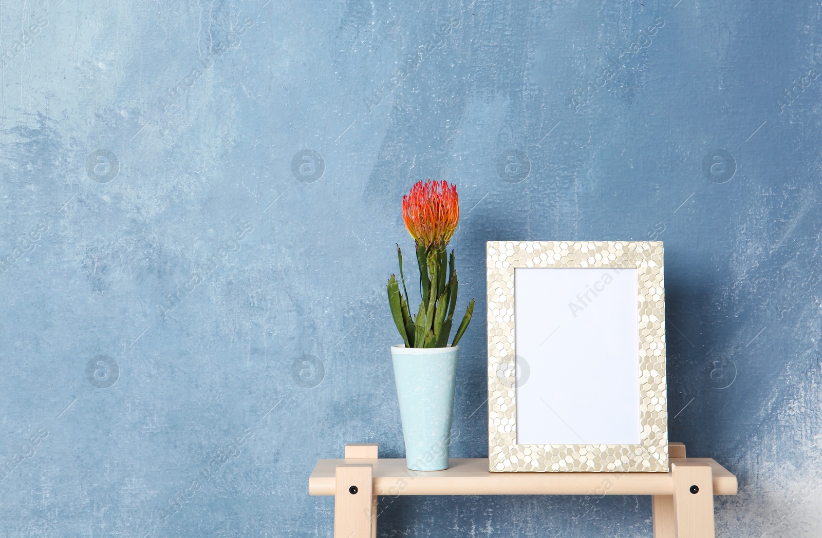 Photo of Blank frame and vase with flower on table near color wall. Mock up for design