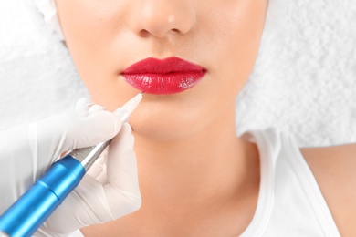 Photo of Young woman getting permanent makeup on lips in beautician salon, closeup