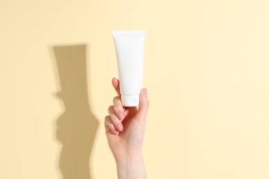 Woman holding tube of cream on yellow background, closeup