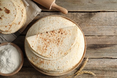 Tasty homemade tortillas, flour, rolling pin and spikes on wooden table, flat lay. Space for text