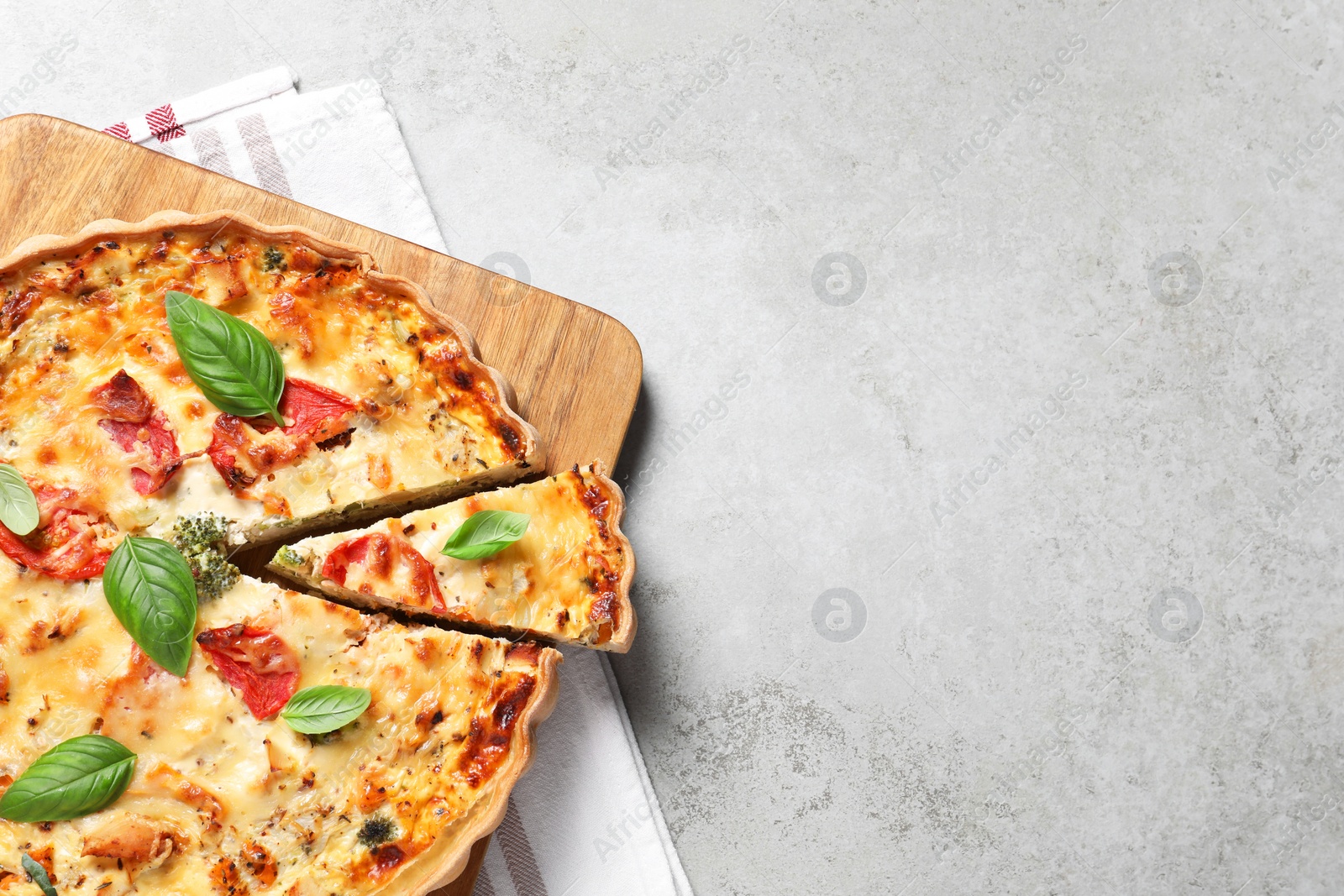 Photo of Tasty quiche with tomatoes, basil and cheese on light textured table, top view. Space for text