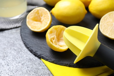 Slate plate with lemon reamer and squeezed fruit on grey table, closeup