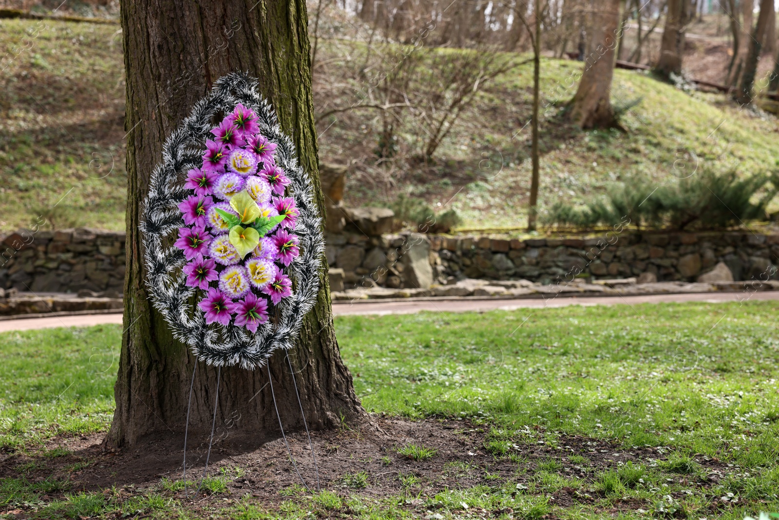 Photo of Funeral wreath of plastic flowers on tree outdoors