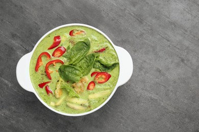 Photo of Saucepan with delicious green curry chicken soup on light grey table, top view. Space for text