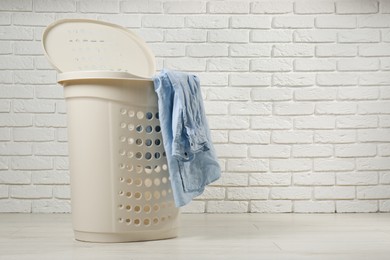 Laundry basket with clothes near white brick wall. Space for text