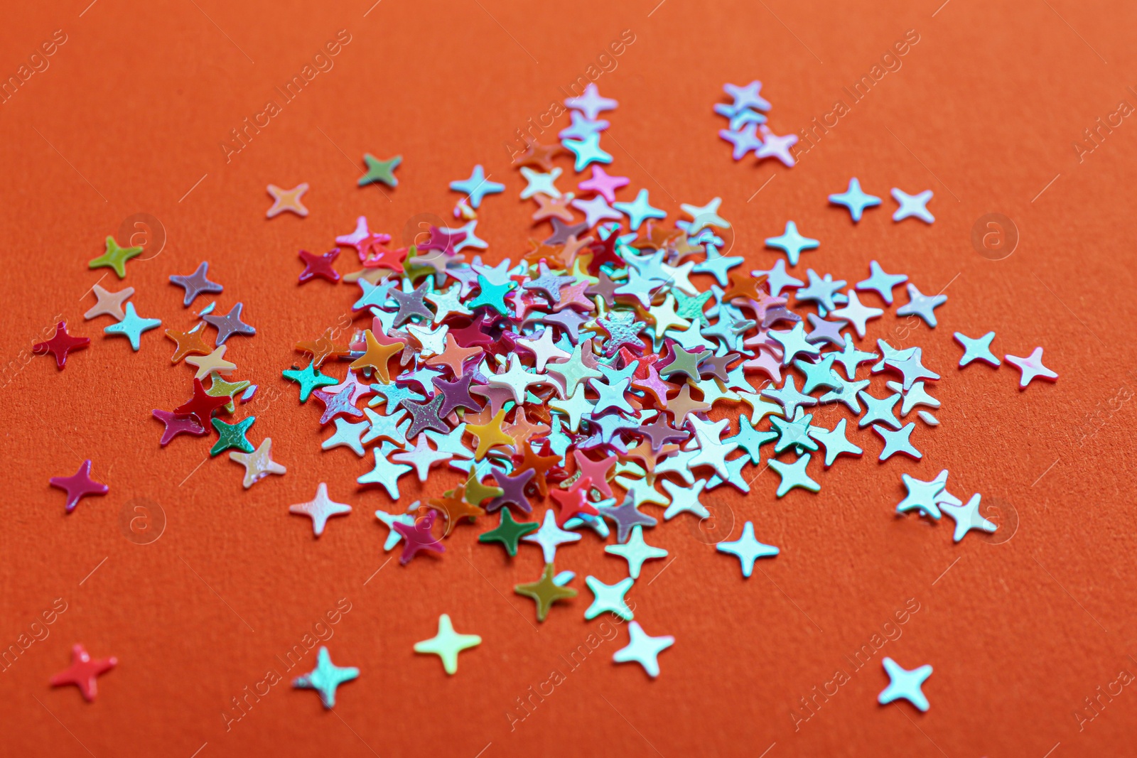 Photo of Shiny bright colorful glitter on orange background, closeup