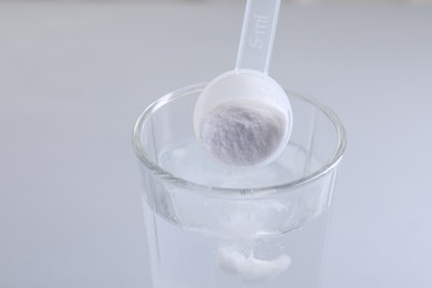 Photo of Adding baking soda into glass of water on light grey background, closeup