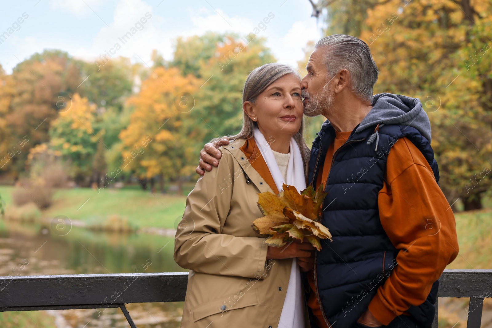 Photo of Affectionate senior couple with dry leaves in autumn park, space for text