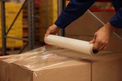 Photo of Worker wrapping boxes in stretch film at warehouse, closeup