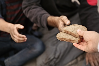 Woman giving poor homeless people pieces of bread outdoors, closeup