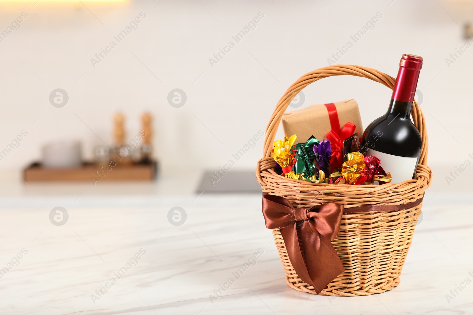 Photo of Wicker basket full of gifts on wooden table in kitchen. Space for text