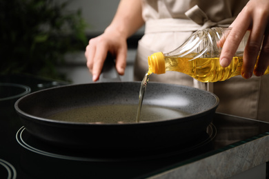 Photo of Woman pouring cooking oil from bottle into frying pan, closeup