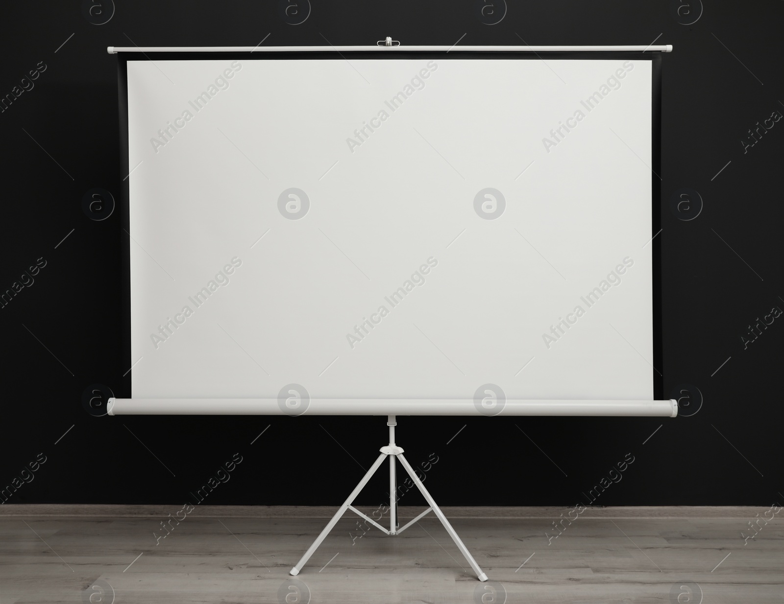 Photo of Blank projection screen near black wall indoors. Space for design