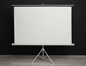 Photo of Blank projection screen near black wall indoors. Space for design