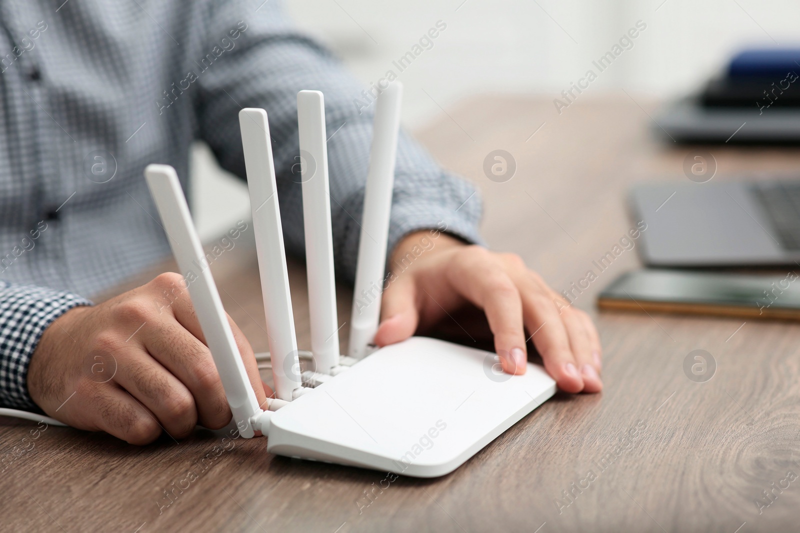 Photo of Man inserting cable into Wi-Fi router at wooden table indoors, closeup