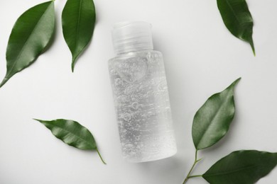 Bottle of cosmetic gel and green leaves on white background, flat lay